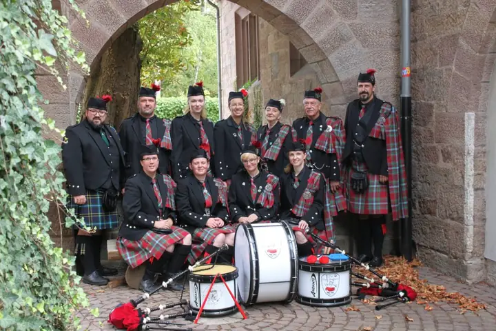 Gruppenfoto der Pipes and Drums of Cherrytown in voller Tracht unter einem steinernen Torbogen