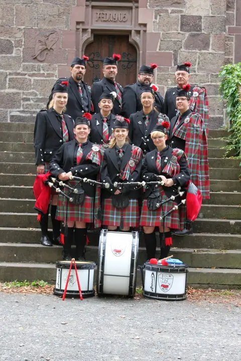 Gruppenfoto der Pipeband mit Dudelsäcken und Trommeln auf einer Steintreppe